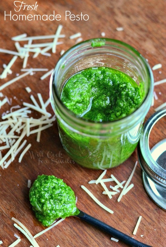 pesto in a jar with some on a spoon on the table and parmesan cheese sprinkled on the table 