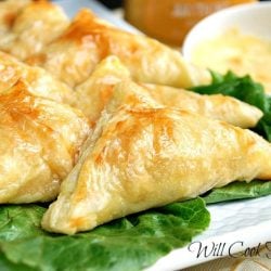 8 triangular shaped honey dijon chicken pockets on a bed of lettuce on white plate with a small sauce bowl in background filled with honey dijun dressing