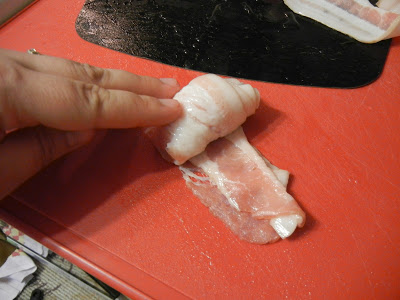 rolling a piece of bacon up on a red cutting board 