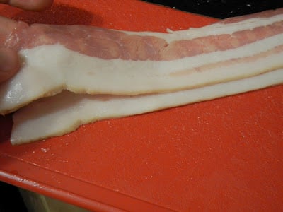two slices of bacon on a red cutting board 