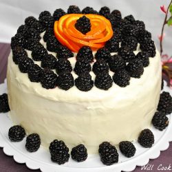 whole blackberry daiquiry cake sitting on a table covered in a purple cloth and decortive branches in the background to the right.