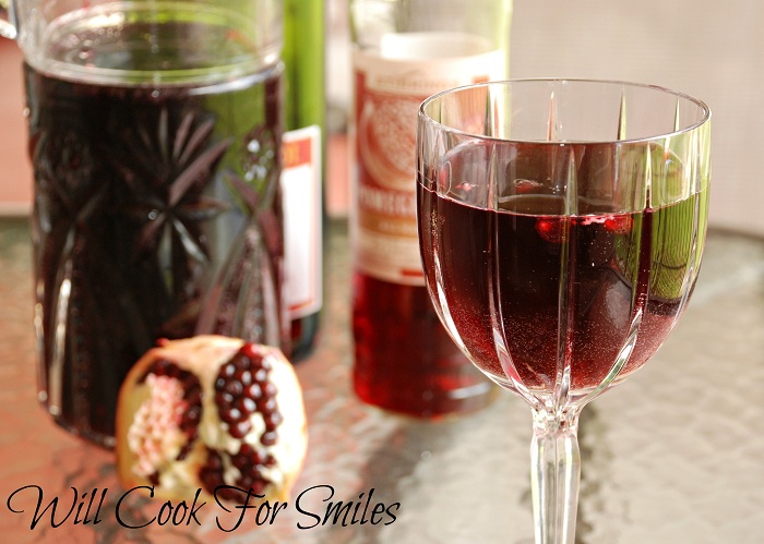 Pomegranate sangria in a wine glass with a slice of pomegranate to the left.