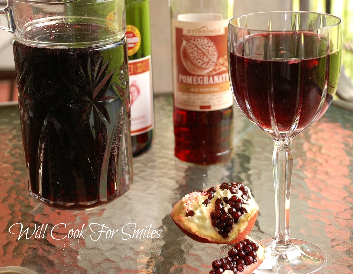 pomegranate sangria in a whine glass with a pomegranate that has been cut in half behind it and the rest of the bottle of sangria 