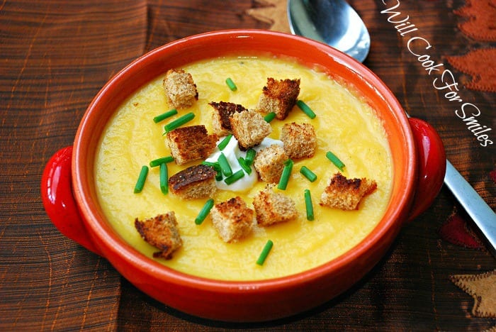  The Best Potato Butternut Squash Soup in a bowl with croutons, sour cream, and chives, on a table with a spoon next to it 