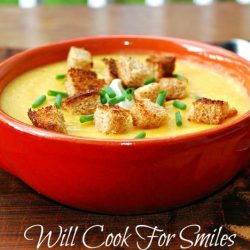 red clay bowl filled with potato butternut squash soup on a fall festive placemat and a silver spoon to the right of the bowl