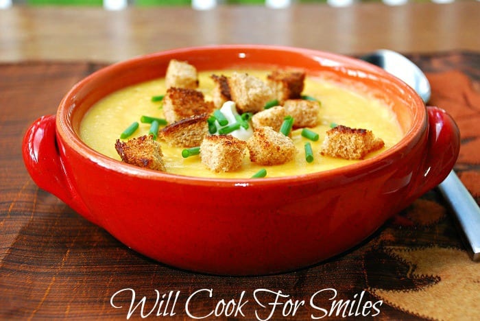red clay bowl filled with potato butternut squash soup on a fall festive placemat and a silver spoon to the right of the bowl