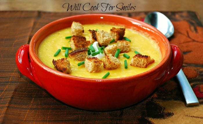  The Best Potato Butternut Squash Soup in a bowl with croutons, sour cream, and chives, on a table with a spoon next to it 