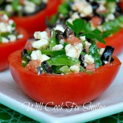 4 stuffed tomato cups on a white rectangular plate on green cloth