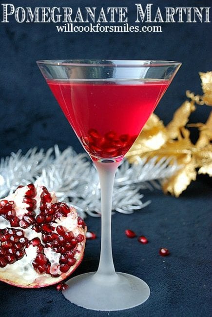 tall martini glass with deep red martini and pomegranates around
