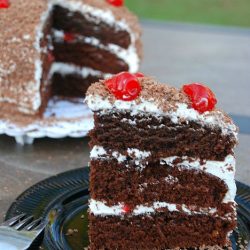 slice of chocoalte case with white frosting and cherries on top on a black plate