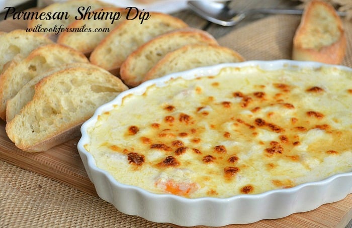 Parmesan shrimp dip in a casserole dish with crusty bread sliced next to it on a cutting board 