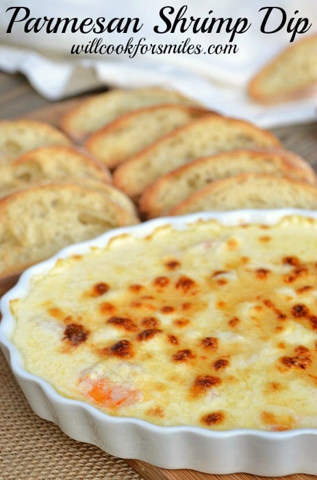 Parmesan shrimp dip in a white baking dish with slices bread behind the bowl on the table 