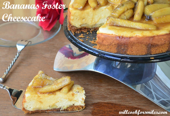 Bananas Foster Cheesecake slice on a pie spatula with a fork and plate to the top left and the rest of the cheesecake on a cake stand to the right 