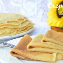 crepes layered and shingled on white plate with fork to the left more crepes on plate in the background