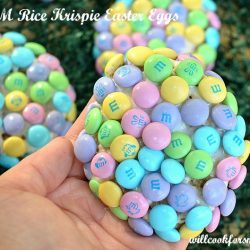 picture of hand holding rice crispy treat egg with m&ms covering it 2 partial crispies in background
