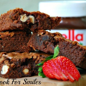 Nutella Brownies with nuts stacked on a wood cutting board with a sliced strawberry in front 
