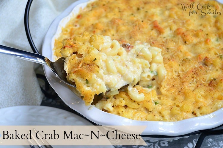 crab mac and cheese on a white plate with a fork in the front and the rest of the mac and cheese in a casserole dish in the background