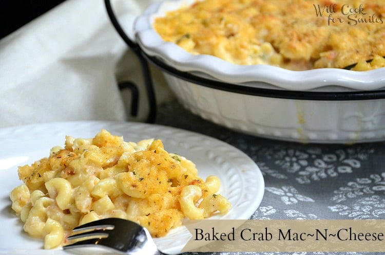 crab mac and cheese on a white plate with a fork in the front and the rest of the mac and cheese in a casserole dish in the background
