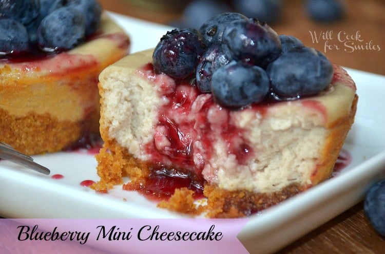 2 mini blueberry cheesecakes on white plate garnished with blueberries and sauce first one cut into