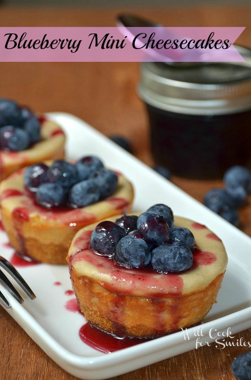 three Blueberry mini cheesecake with blueberries on top on a white dish with a bite out of it 