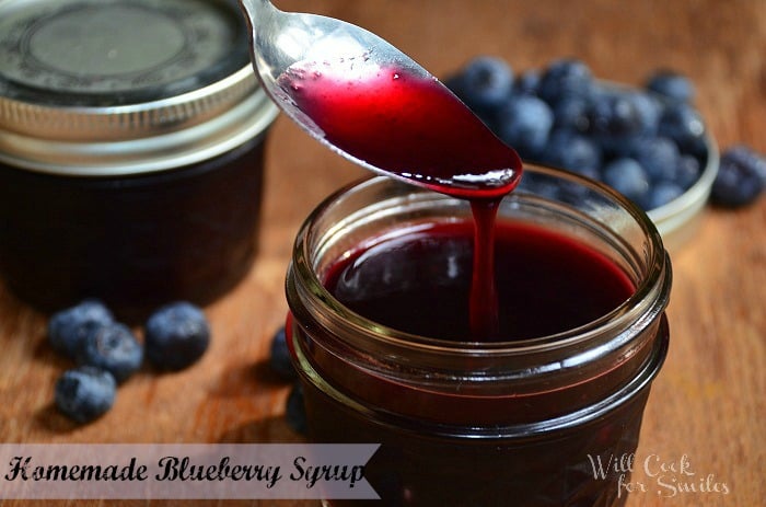 spooning blueberry syrup in a small mason jar on a wood table 