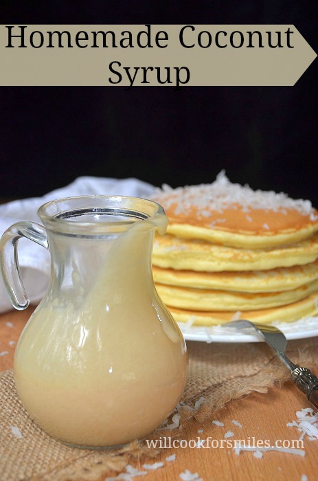 glass jar with homemade coconut syrup on burlap cloth with stack of coconut topped pancakes and fork in the background to the right