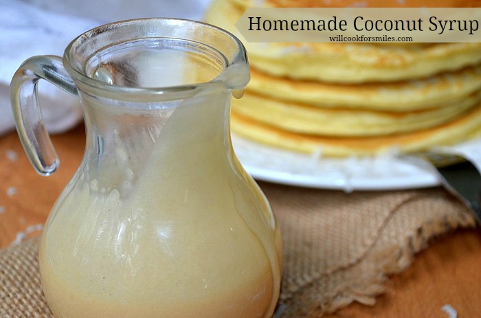 glass jar with homemade coconut syrup on burlap cloth with stack of coconut topped pancakes and fork in the background to the right