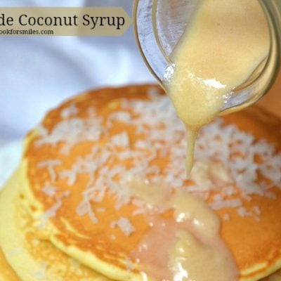 Coconut syrup being poured over stack of pancake that has coconut shaving on top
