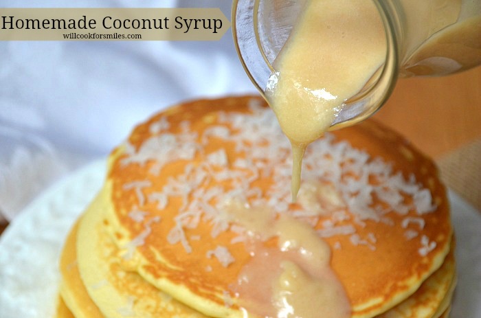 glass jar with coconut syrup being poured over a stack of coconut topped pancakes 