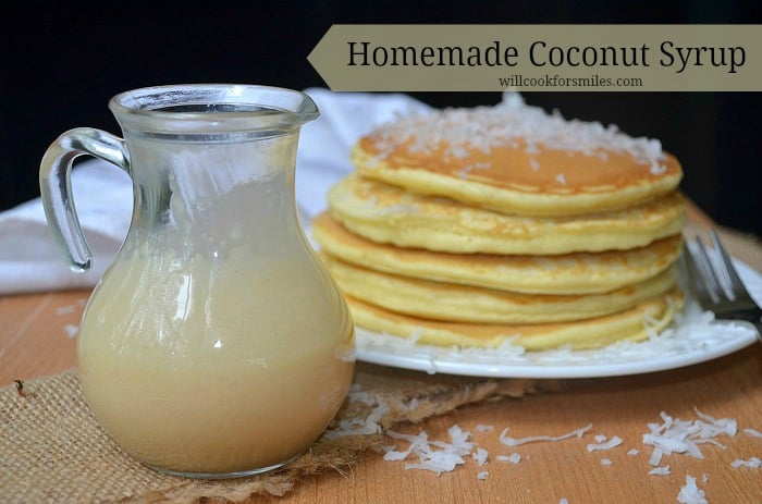 glass jar with homemade coconut syrup on burlap cloth with stack of coconut topped pancakes and fork in the background to the right