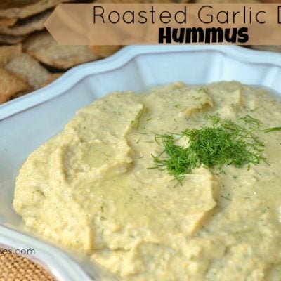 mound of roasted garlic dill hummus in white bowl with bag of chips to back left close up