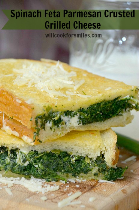 Spinach Feta Parmesan Crusted Grilled Cheese cut in half on a wood cutting board 