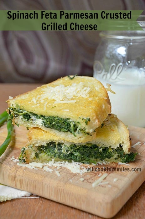 SPinach feta parmesan grilled cheese cut in half staked one each other with 1 greenonion to the left resting on wood cutting board glass of milk in back ground