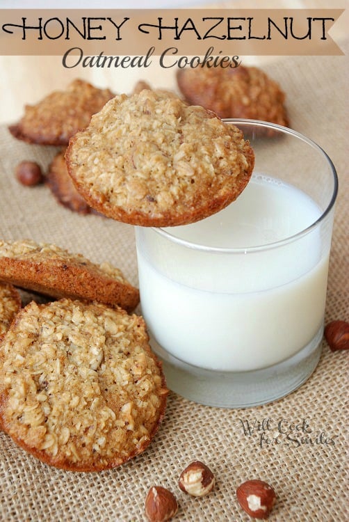 Hazelnut Honey Oatmeal cookies stacked up and a glass of milk to the left with a cookie on the glass 