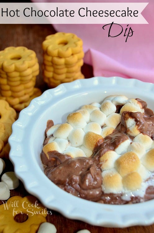 hot chocolate cheesecake dip in a white bowl with cookies stacked up to the left of it 