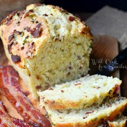 sliced bacon cheese savory bread on a wood cutting board with 2 slices of bacon to the left