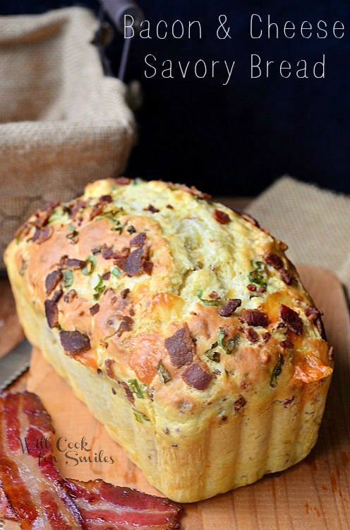 whole loaf of bacon cheese savory bread with 2 slices of bacon to the left on a cutting board shot from front and slightly above