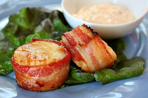 two bacon wrapped scallops on a plate on top of lettuce 