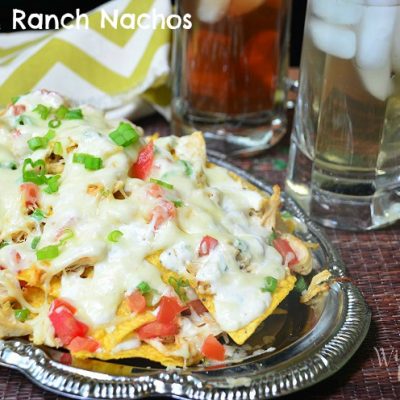 front shot of chicken ranch nachos on silver platter with 2 drinks in glasses in background to the right