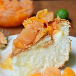 slice of cake with citrus topping on white plate with fork and clear glass bowl of citrus salsa topping in background