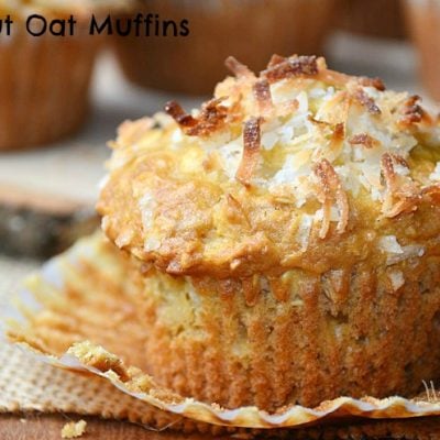 shot from front close up of muffin with live wood tray with several coconut oat muffins