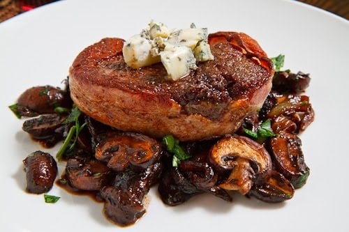 shot from front and slightly above filet mignon resting on top of mushrooms on white plate