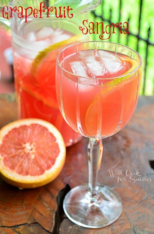 shot from front and slightly above 1 glass of grapfruit sangria with a cut grapefruit below to left and a full pitcher of sangria in background to the left