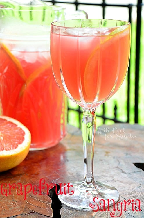 Grapefruit-Sangria in a wine glass on a table with a picture of sangria in the background with slice of grapefruit. 