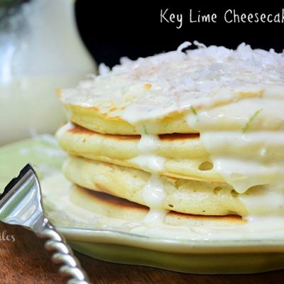 key lime cheesecake pancakes stacked on decorative lime green plate and fork with bottle of syrup in background to the left shot from front