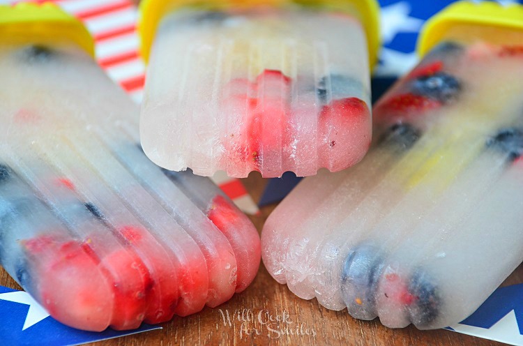 side few of red white and blue ice pops on a wood table with red and white stripped flag and blue flag with stars 