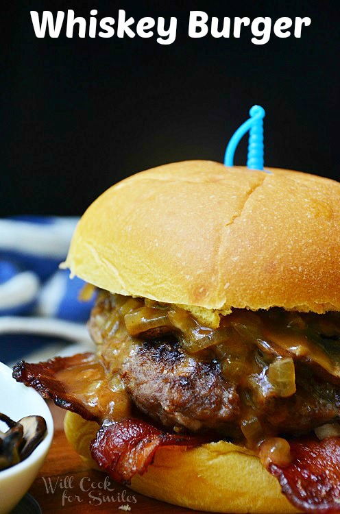 1 whiskey burger in wood cutting board with small white bowl sauce and of mushroom to the left