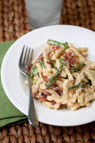 bacon asparagus pasta in a white bowl with a fork to the left 