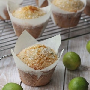 key lime muffin on a table with the rest on a cooling rack and little limes around it 