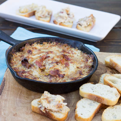 black skillet of baked onion dip shot from above with sliced bread for dipping around the skillet